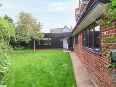 A backyard with grass and a tree next to a brick house with black window frames at Town Farm House Orford