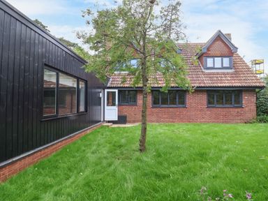 A backyard with a tree lawn a brick house with multiple windows and a black wooden extension at Town Farm House Orford