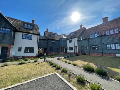 A courtyard with a pathway and bushes in front of residential buildings at Corner Cottage Thorpeness