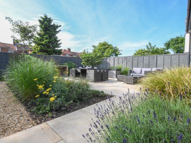 A garden patio with outdoor seating and dining furniture surrounded by plants and fenced yard at Corner Cottage Thorpeness