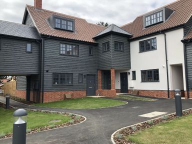 A residential building with gray and white walls, multiple windows, and a tiled roof with pathways and grass at Corner Cottage Thorpeness