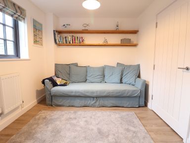 A snug with a sofa and shelf containing books at Corner Cottage, Thorpeness