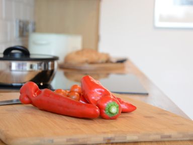 Red bell peppers and cherry tomatoes on a wooden cutting board in a kitchen at Fishpond House Sotherton Halesworth