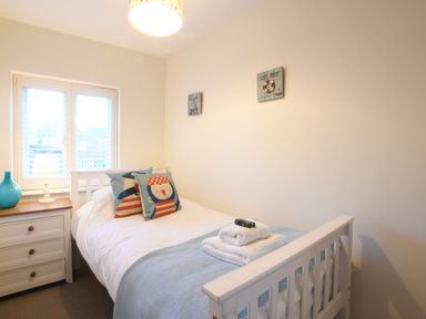 A bedroom with a single bed pillows bedside table with lamp and blue vase at Smugglers Rest Aldeburgh