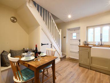 A kitchen with a dining table set under stairs and a door near a sink at Smugglers Rest Aldeburgh