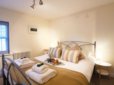 A bedroom with a bed with striped pillows and folded towels on it with bedside tables and lamps at Smugglers Rest Aldeburgh