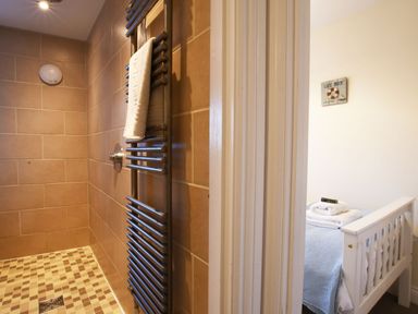 A bathroom with a tiled shower and heated towel rail next to a bedroom with a white bed frame at Smugglers Rest Aldeburgh