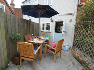 An outdoor patio area with a wooden table and four chairs under a large blue umbrella at Smugglers Rest Aldeburgh