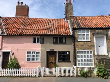 A row of three old houses with tiled roofs and chimneys behind white picket fences at Rosemary Cottage Aldeburgh