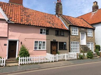 A row of three cottages with orange tiled roofs white picket fences and small front gardens at Rosemary Cottage in Aldeburgh
