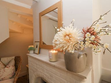 A fireplace mantel with a candle a small plant a framed picture and a vase with flowers and a mirror above at Rosemary Cottage Aldeburgh