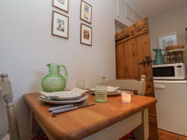 A small dining table set with dishes glasses and utensils next to a wooden door in a kitchen area at Rosemary Cottage Aldeburgh