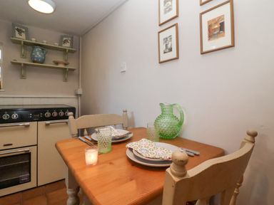 A small kitchen dining area with a wooden table set for two near a stove and green shelves on the wall at Rosemary Cottage Aldeburgh