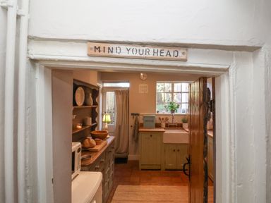 A kitchen with wooden cabinets a bread bin a sink and shelves with dishes at Rosemary Cottage in Aldeburgh