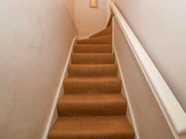 A narrow staircase with a beige carpet and white handrail at Rosemary Cottage Aldeburgh