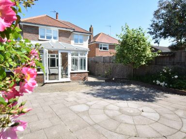A backyard with paved circular patio area a conservatory on a brick house and plants including a tree and flowers at Napier House Southwold