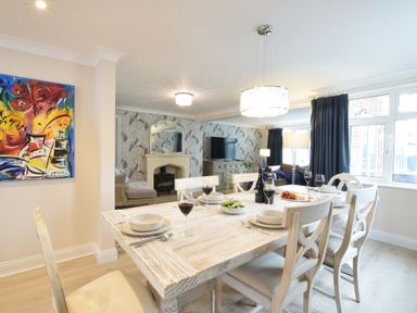A dining area with a wooden table set with bowls glasses and wine bottles next to a living room with a fireplace and television at Napier House Southwold