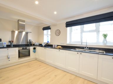 A kitchen with white cabinets black countertops a stainless steel oven and sink at Napier House Southwold