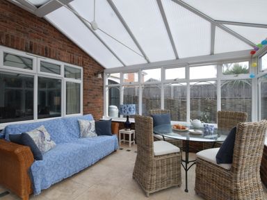 A conservatory with wicker furniture including a sofa and chairs around a glass dining table at Napier House Southwold