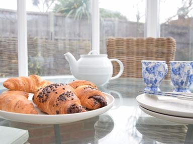 A glass table with croissants on a plate a white teapot two blue and white cups and plates with cutlery at Napier House Southwold