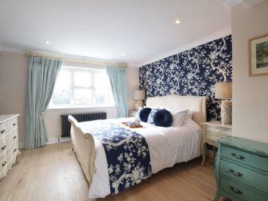 A bedroom with a bed with blue and white bedding and patterned wallpaper at Napier House Southwold