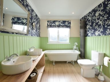 A bathroom with two sinks on a wooden countertop a freestanding bathtub a toilet and floral wallpaper at Napier House Southwold