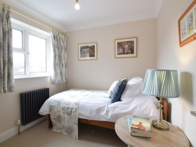 A bedroom with a single bed beside a window and a round wooden side table with a lamp and books at Napier House Southwold