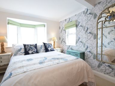 A bedroom with a bed between two lamps a green chest under a window and wallpaper with bird designs at Napier House Southwold