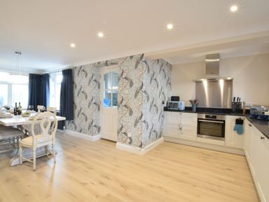 A kitchen with white cabinets a stainless steel oven dining table and chairs near windows with dark curtains at Napier House Southwold