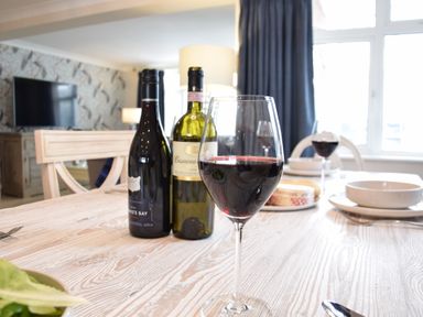 A dining table with two bottles of wine and glasses filled with red wine at Napier House Southwold