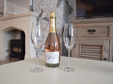 A bottle of Adnams fizz rose wine with two empty wine glasses on a table in a room with a fireplace and a wooden cabinet at Napier House Southwold