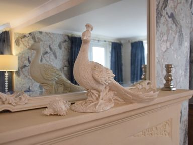 A decorative bird sculpture and a shell on a mantelpiece with a mirror and patterned wallpaper at Napier House Southwold