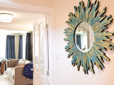 A decorative sunburst mirror on the wall near an open door showing a beige sofa and curtains in the living room at Napier House Southwold