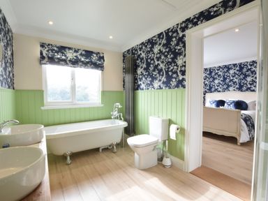 A bathroom with a bathtub toilet double sinks and floral wallpaper connected to a bedroom at Napier House Southwold