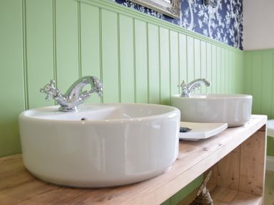 Two white round sinks with chrome faucets on a wooden countertop against a green paneled wall at Napier House Southwold