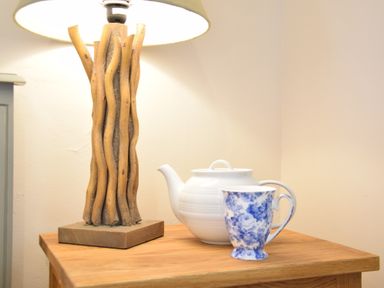 A wooden table with a lamp that has a wooden base a white teapot and a blue and white floral cup at Napier House Southwold