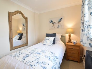 A bedroom with a single bed bedside table lamp large mirror and floral curtains at Napier House Southwold