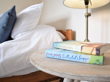 A bedside table with two books and a lamp next to a bed with white and blue pillows at Napier House Southwold