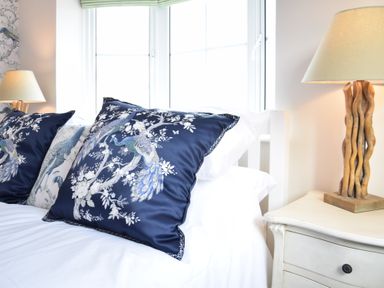 A bed with two decorative peacock pillows and a wooden lamp on a bedside table at Napier House Southwold