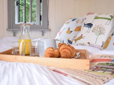 A breakfast tray with croissants orange juice and a white jug on a bed with animal print cushions at Shepherds Pightle in Hollesley