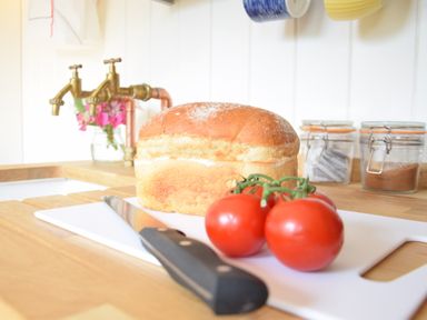 A kitchen counter with a loaf of bread tomatoes a knife and jars in the background at Shepherds Pightle in Hollesley