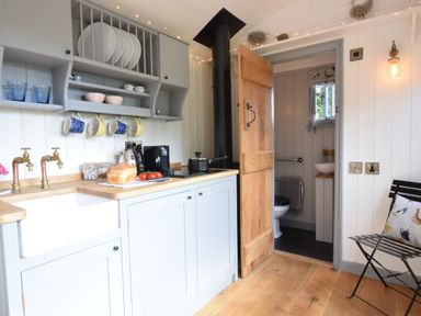 A kitchen area with a sink wooden countertop plates mugs and a wooden door leading to a bathroom at Shepherds Pightle in Hollesley