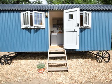 A blue corrugated metal shepherds hut with open white door and windows on wheels at Shepherds Pightle in Hollesley
