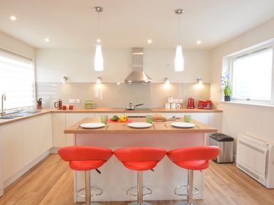 A kitchen with an island and three red stools at Bramertons Nest Long Melford
