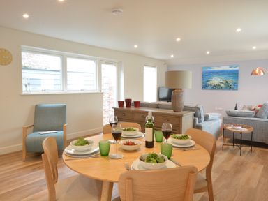 A dining table set with plates bowls of salad glasses of wine and a bottle in a living room with sofas a lamp and a painting at Bramertons Nest Long Melford