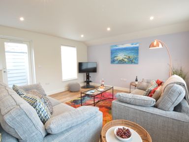 A living room with two gray sofas a colorful rug a coffee table with plates and drinks and a wall-mounted tv at Bramertons Nest Long Melford