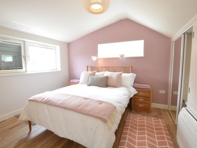 A bedroom with a bed with multiple pillows bedside tables and a rug at Bramertons Nest Long Melford