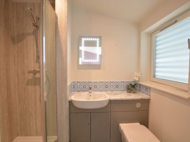 A bathroom with a shower, sink with a mirror, tiled backsplash, and a window at Bramertons Nest Long Melford