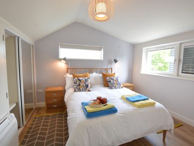A bedroom with a double bed two bedside tables wall lamps a window and folded towels on the bed at Bramertons Nest Long Melford
