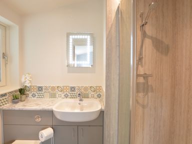 A bathroom with a sink, a lighted mirror, a shower with a glass door, and decorative tiles at Bramertons Nest, Long Melford